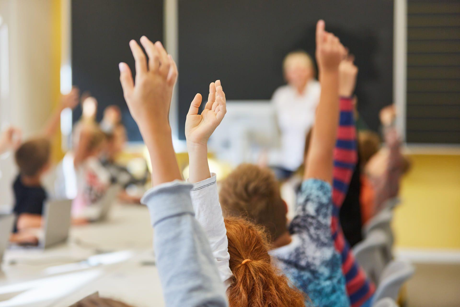 Muchos niños y su profesora en el aula de una escuela, levantando la mano para participar de la clase