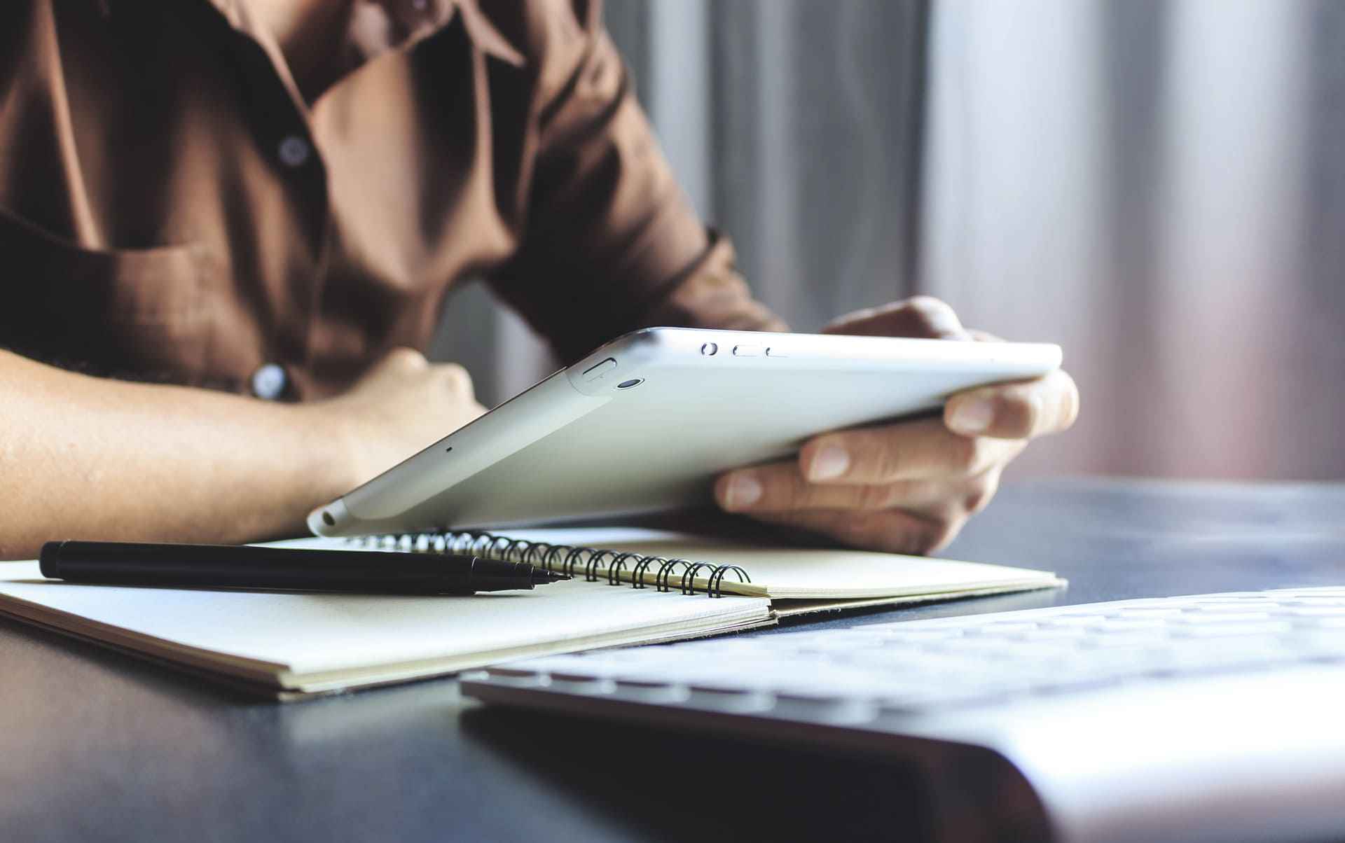 Persona en un escritorio con una libreta para tomar notas, mirando una tablet